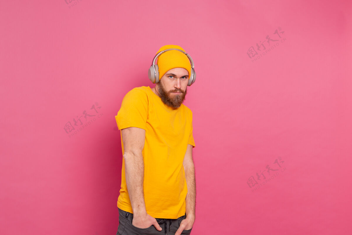 家伙帅哥在随意地听着音乐 用耳机隔离在粉色背景上快乐播放列表男人