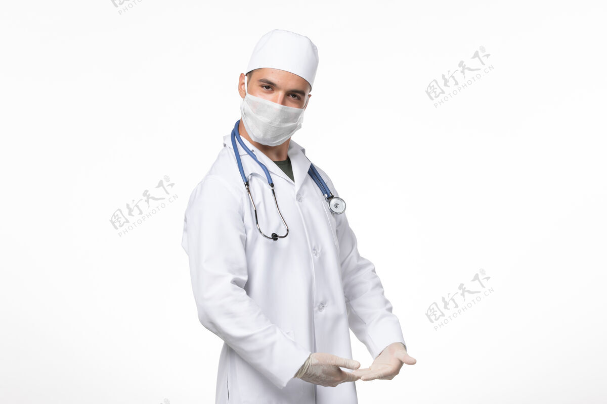 医生正面图：男医生穿着医疗服 戴着口罩 在白色墙壁上摆着柯维德病毒大流行病毒病的姿势视图冠状病毒冠状病毒防护