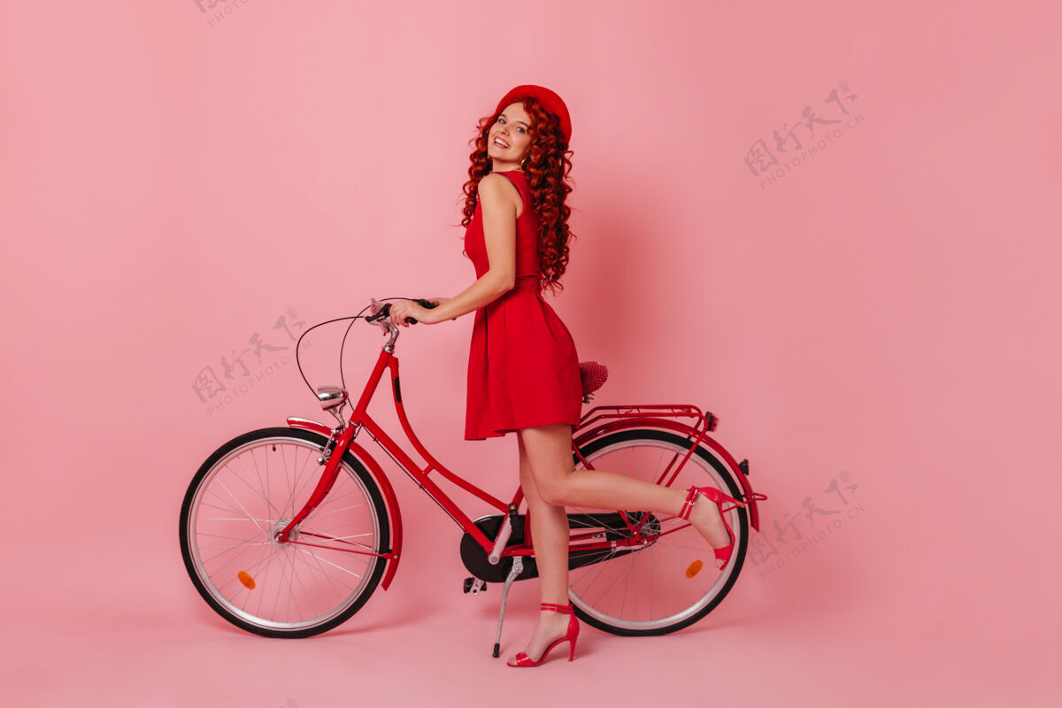 别致长着红色卷发的女孩笑着 撒娇地抬起腿 在与世隔绝的空间里抱着红色女士的自行车帽子性感优雅