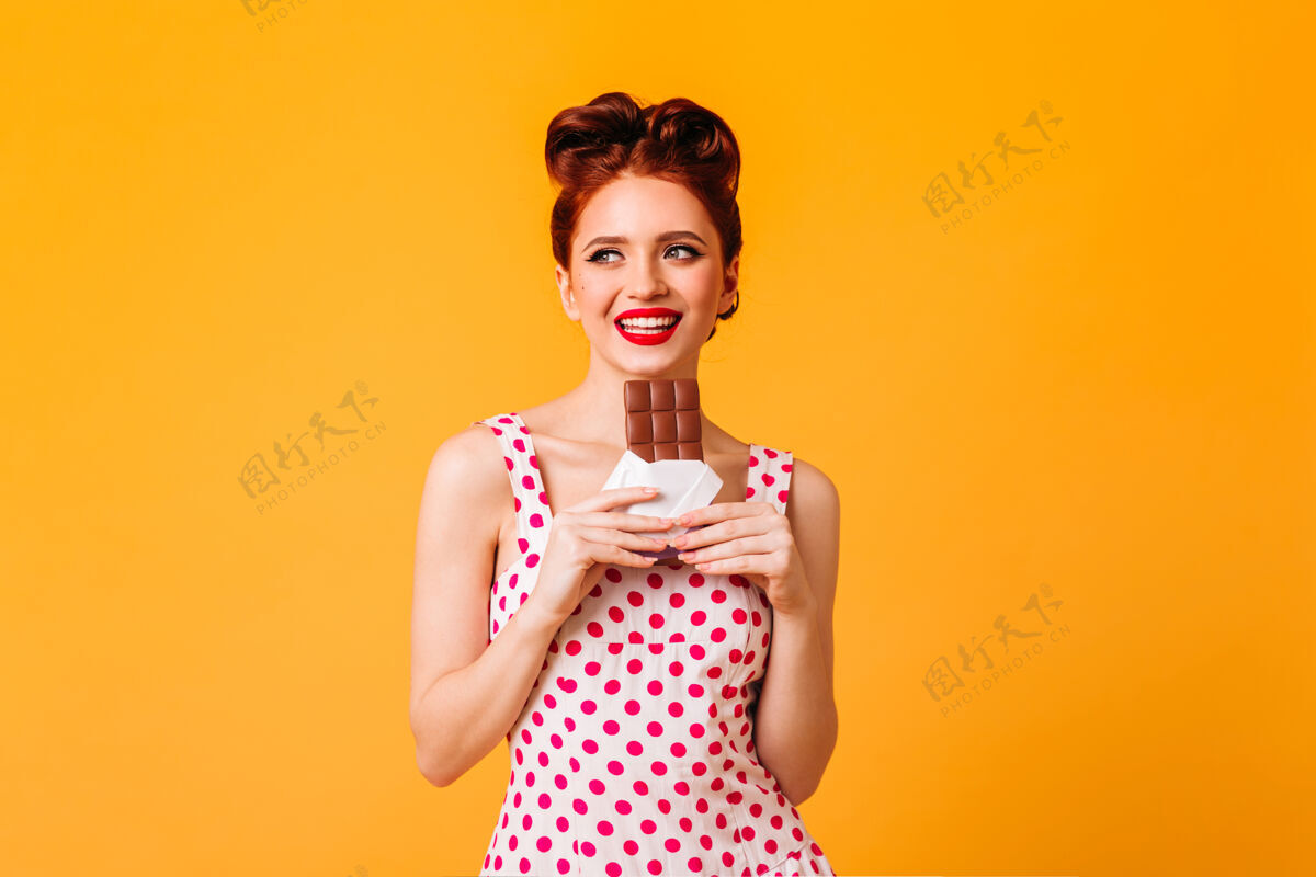 化妆品一个很幽默的欧洲女孩在吃巧克力一个穿着圆点裙的年轻女人在黄色的空间里微笑甜点复制空间连衣裙