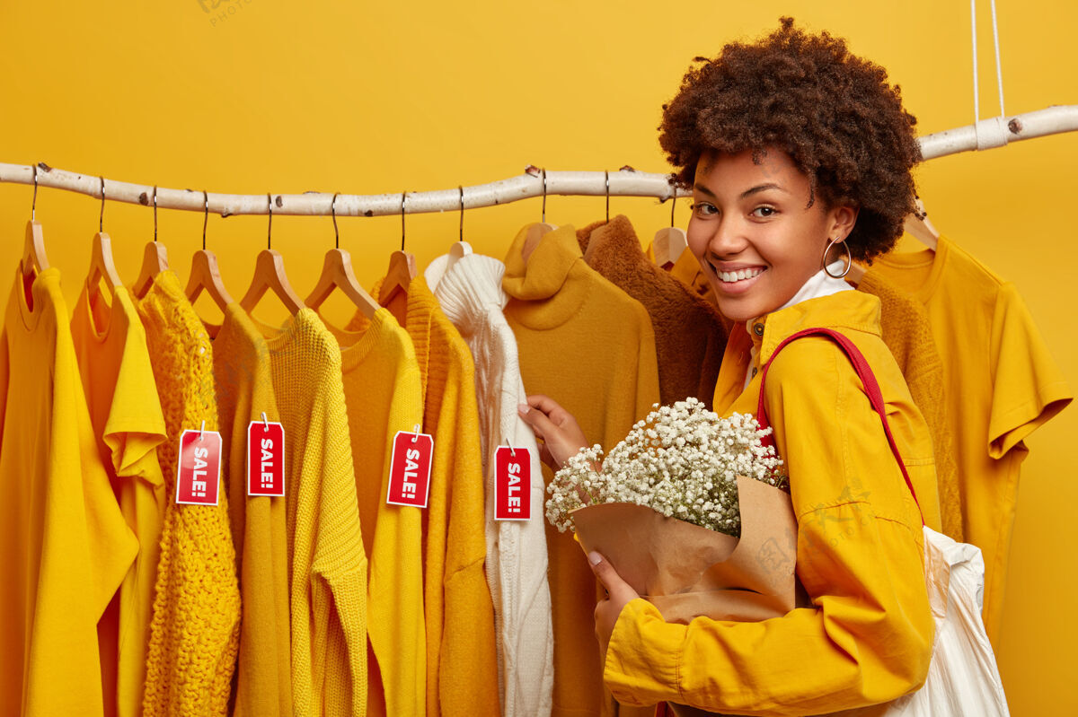 成人购物生活方式概念积极的女性购物者周末在时尚商店 手持花束 站在衣架附近大甩卖毛衣零售选择
