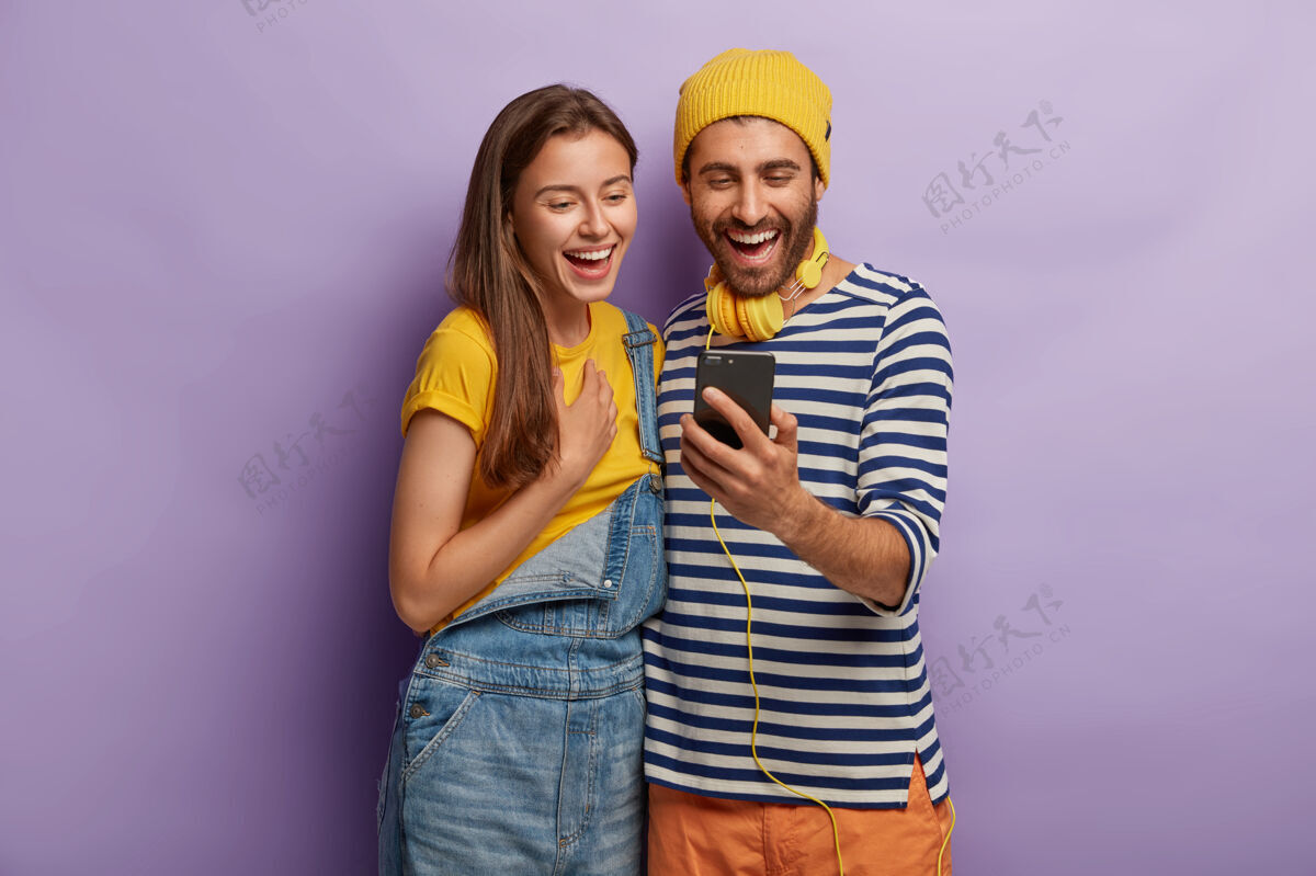 两个快乐的朋友们在一起度过业余时间的照片 在智能手机上看一些东西 彼此站得很近年轻打字电话