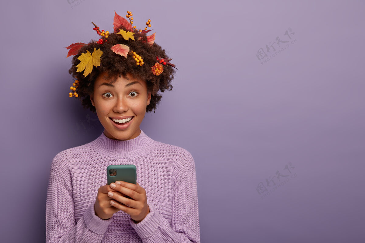 紫色可爱的黑皮肤女孩拿着现代手机 直视镜头 准备打电话 开心地笑着 穿着休闲装 秋天的时候摆姿势 隔离在紫色的墙上黑色秋天欣喜若狂