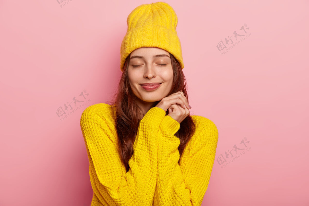 女人可爱的年轻欧洲女人的肖像闭上眼睛 穿着鲜艳的黄色针织毛衣和头饰 隔离在粉红色的背景上白种人服装请