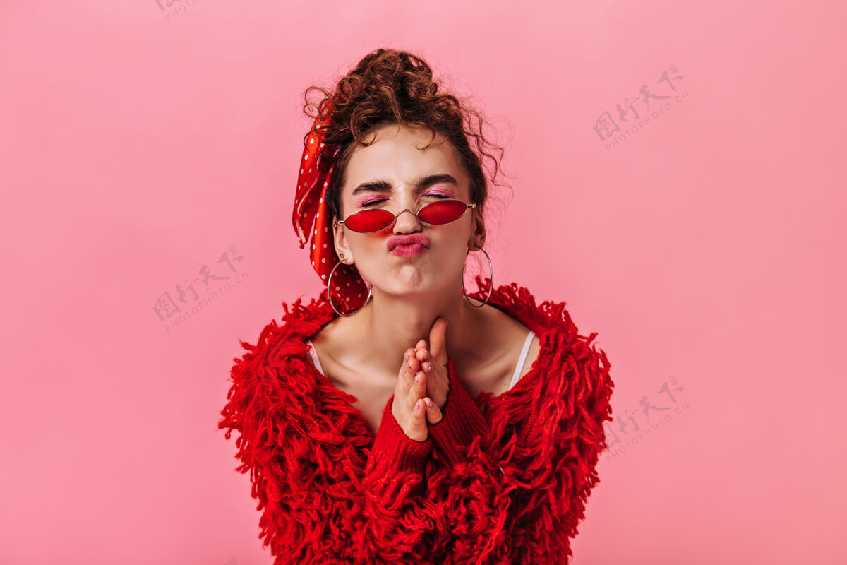愿望一个穿着红色服装 戴着时髦眼镜的女人 在粉色背景上做着一张滑稽的脸生活方式毛衣自信