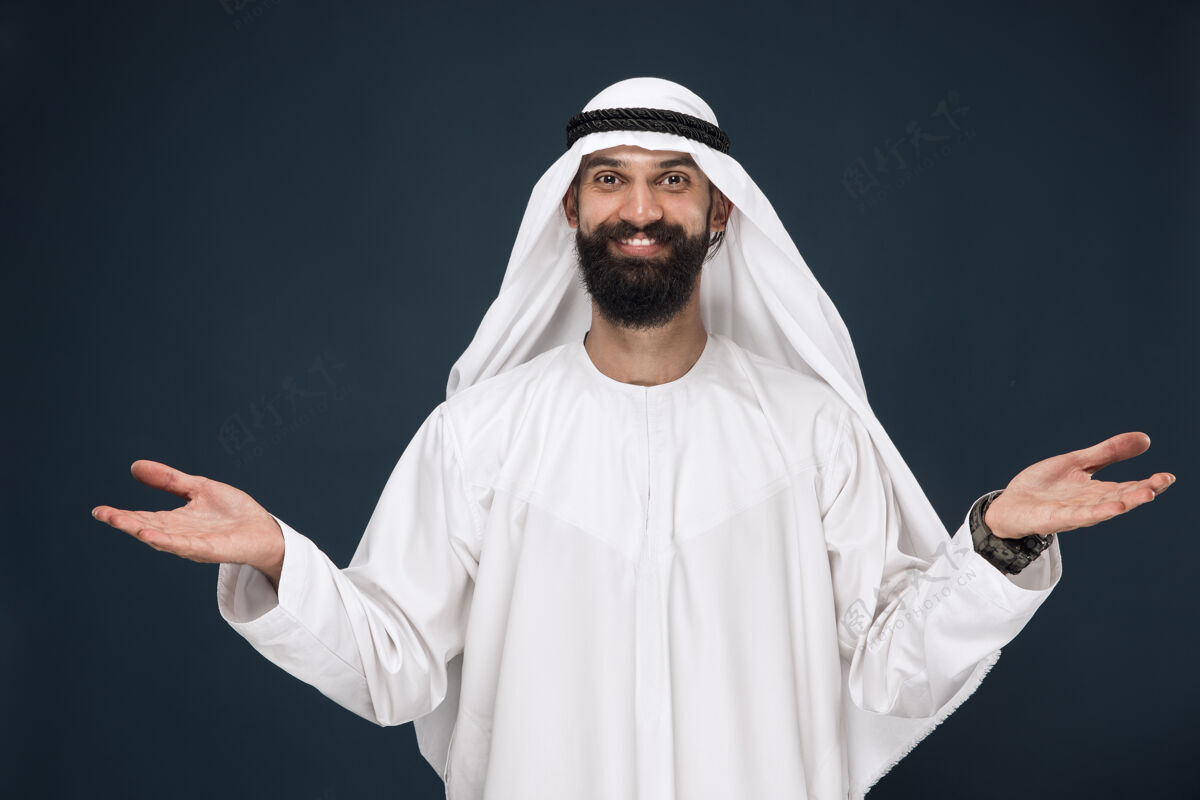 男性深蓝色墙上的半身阿拉伯沙特商人肖像年轻的男模微笑着 展现出邀请的姿态商业概念 金融 面部表情 人类情感情感搞笑意外
