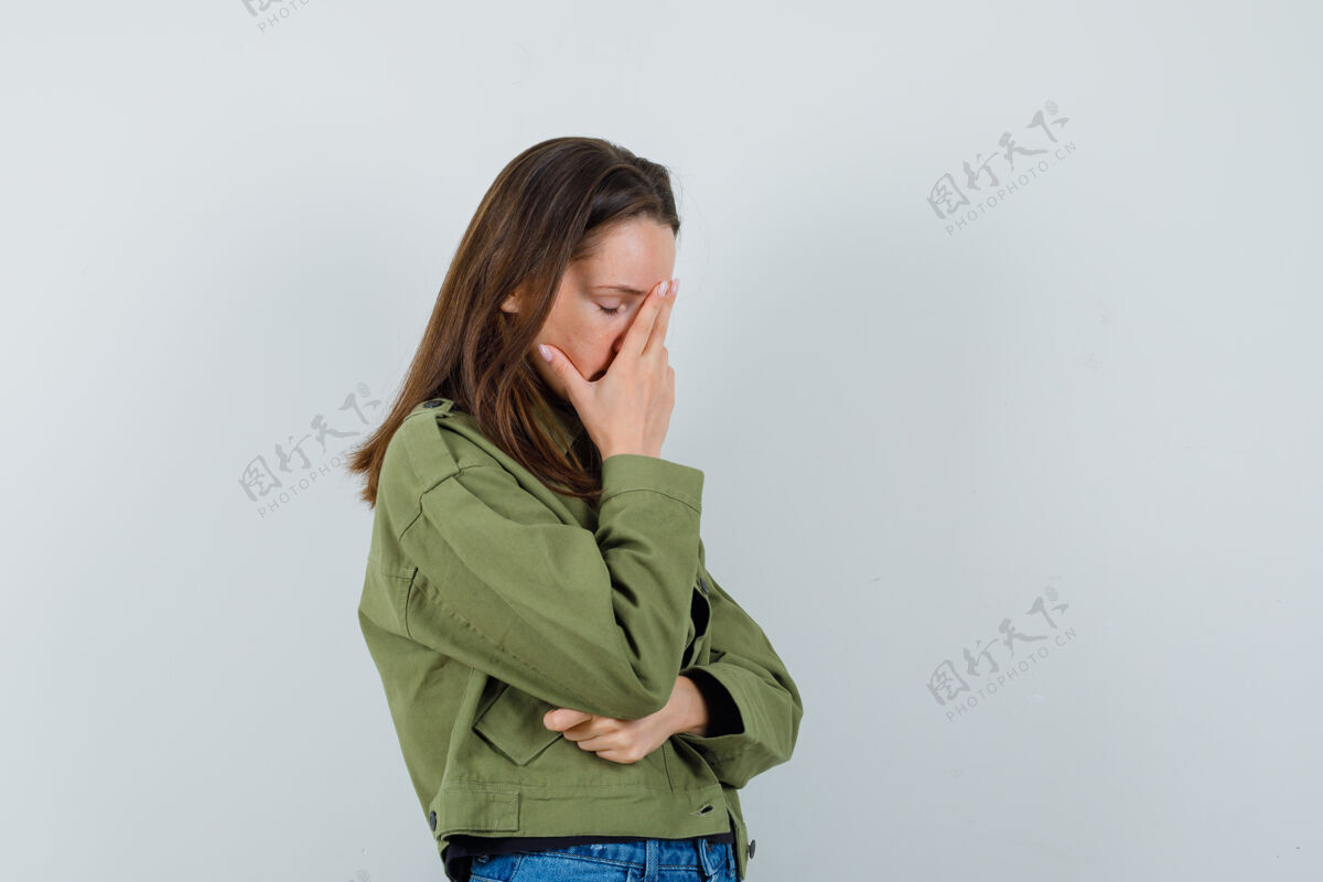 夹克一个穿着绿色夹克的年轻女人 手放在脸上 看起来很无聊年轻积极成人