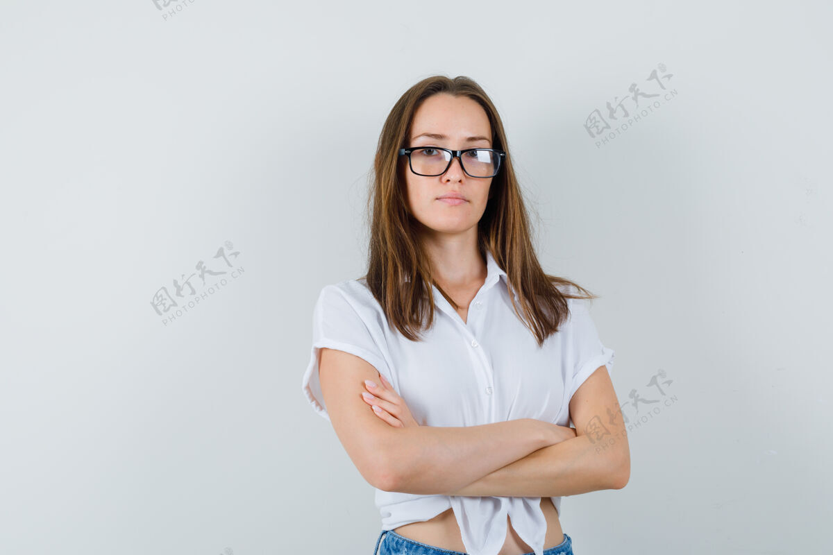 时尚穿着白衬衫的漂亮女士 戴着眼镜交叉着双臂站着 看上去很专注 俯瞰前方年轻站立卷发
