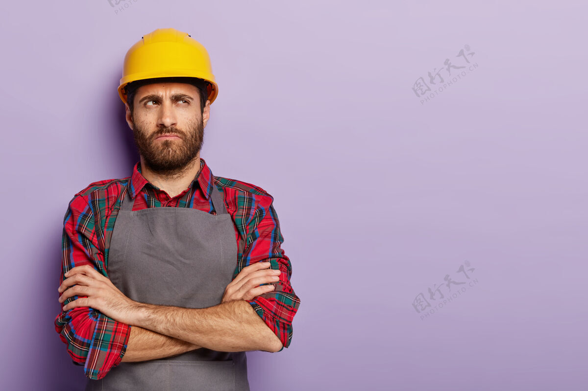 手臂郁闷不满的产业工人镜头戴着黄色安全帽和围裙休闲头盔工业