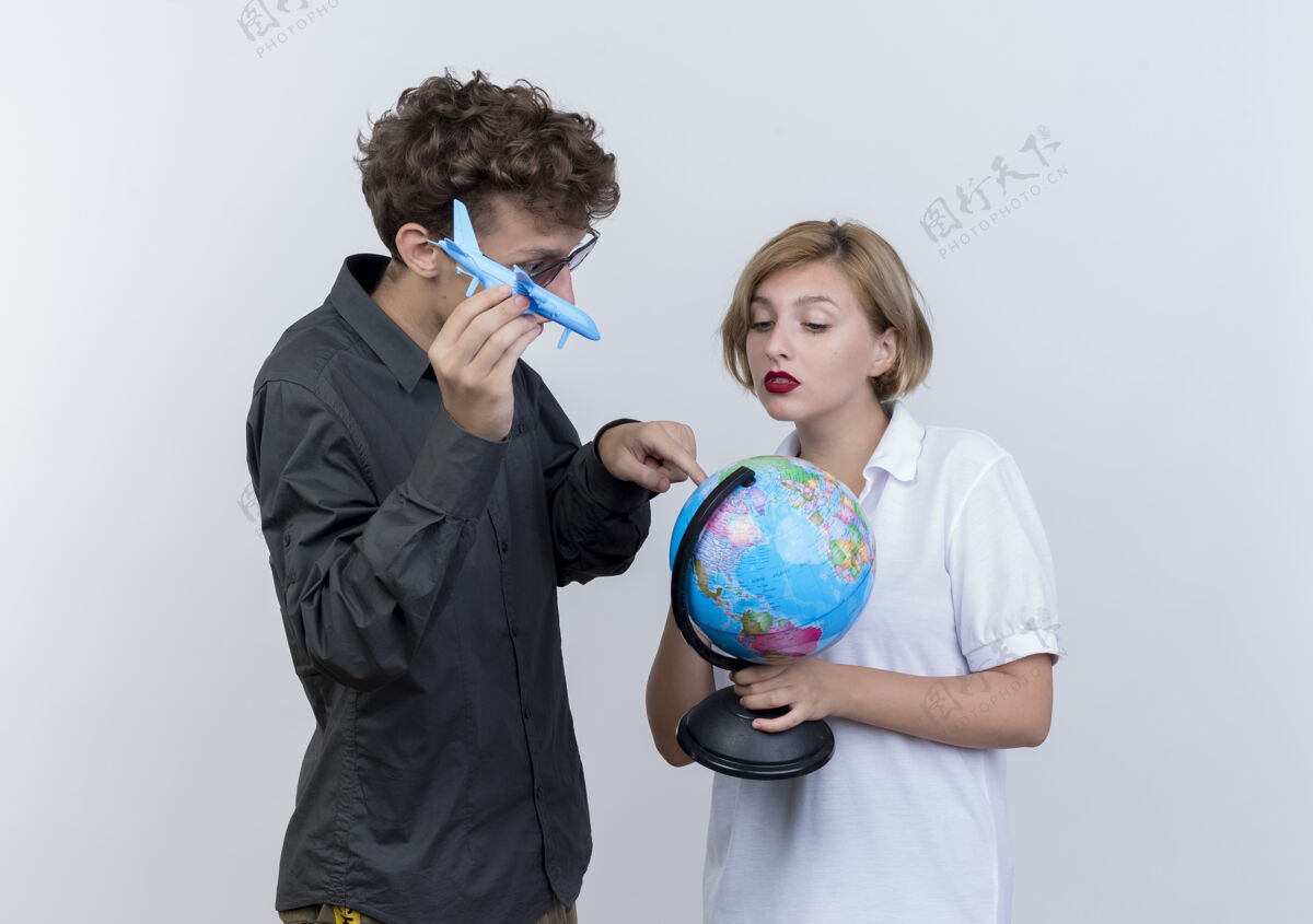 在一起一对幸福的年轻游客男女手持地球仪和玩具飞机一起站在白墙上空中情侣抱着
