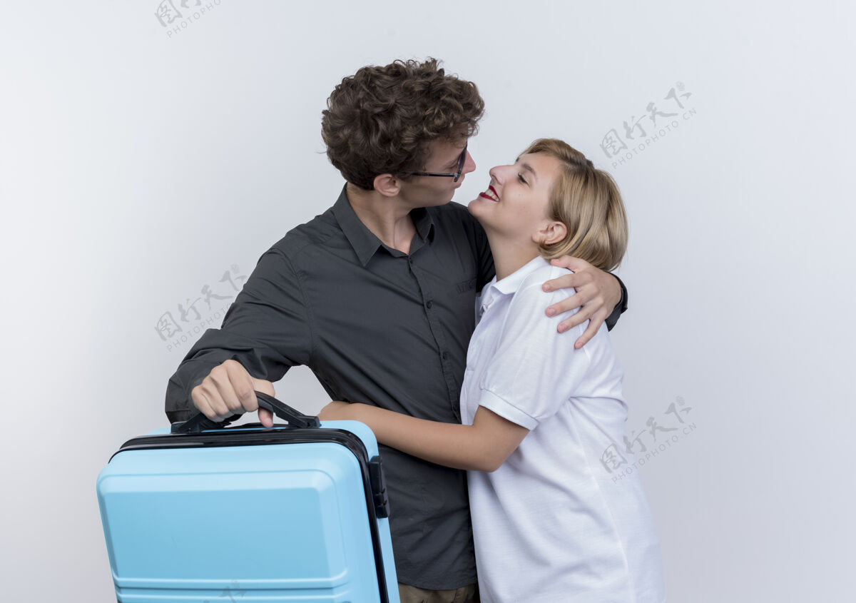 年轻人一对快乐的年轻游客 一男一女拿着手提箱 隔着白墙互相拥抱 看着对方抱着夫妇手提箱