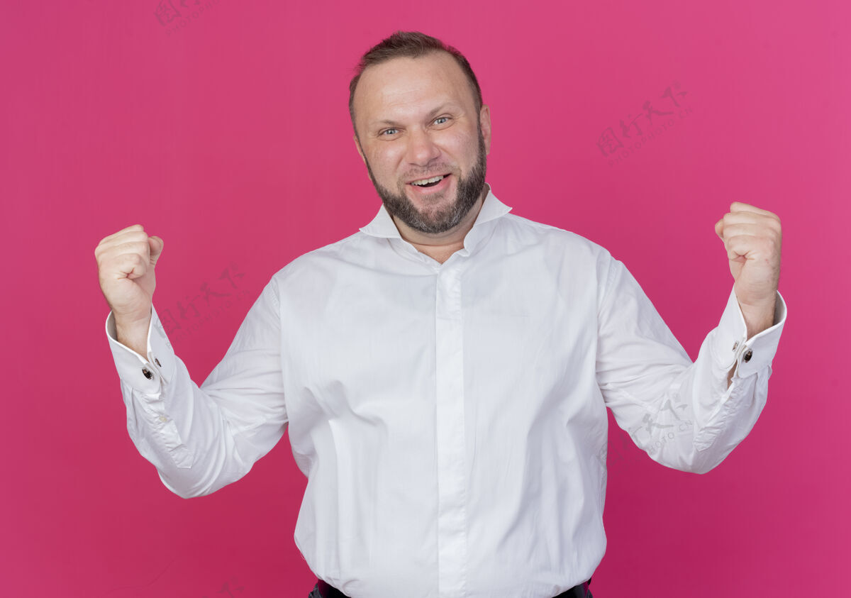 兴奋一个留着胡须 身穿白衬衫 握紧拳头的男人站在粉红色的墙上 为自己的成功感到高兴和兴奋握紧男人穿