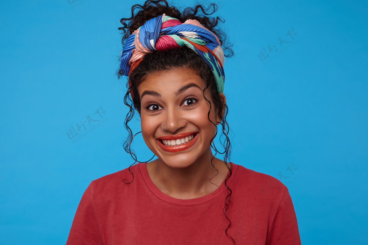 聚会年轻快乐的黑发女人 卷曲的头发 微笑着看着镜头 穿着彩色衣服站在蓝色的背景上站姿蓝色情绪