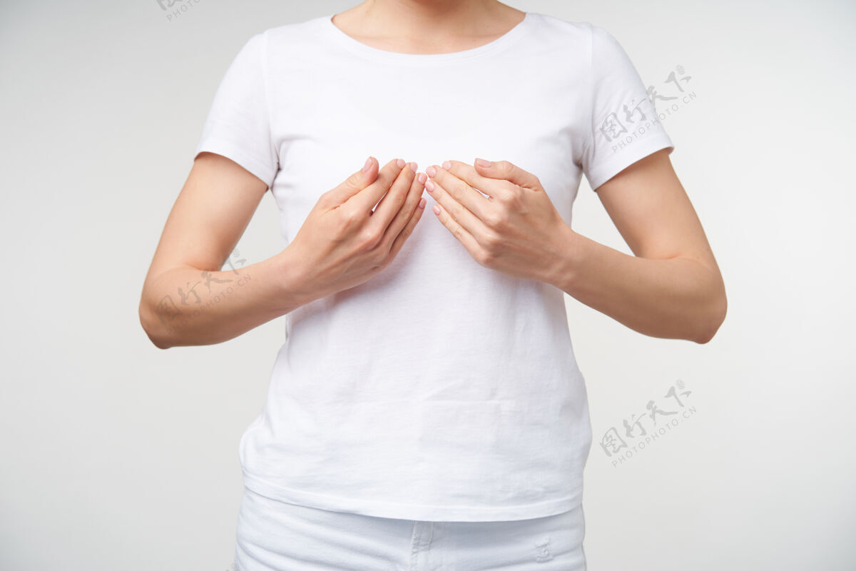 年轻摄影棚拍摄的一张照片 身着白色t恤的年轻女性一边学习手语 一边站在白色背景上 一边将手掌放在胸前 一边展示单词书手臂皮肤白皙文字