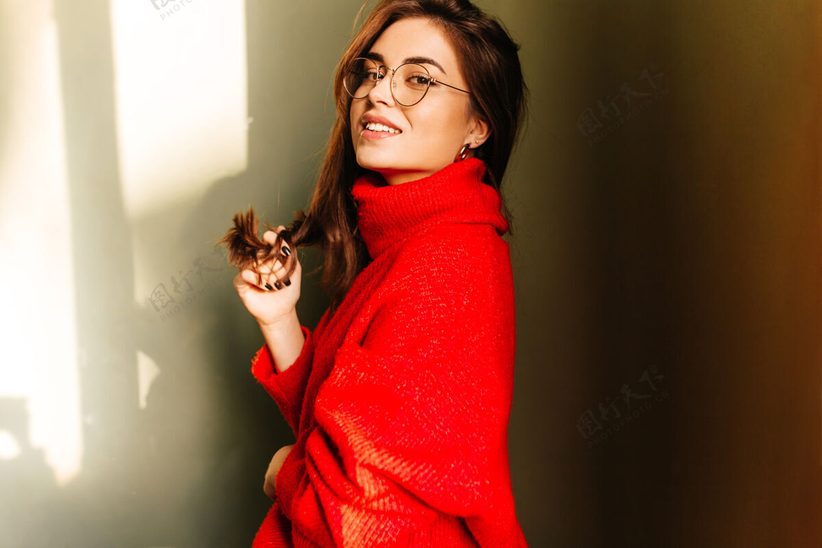 肖像戴着眼镜 穿着红色针织毛衣 在白墙上微笑的黑发女孩的特写镜头情绪红色毛衣黑眼睛