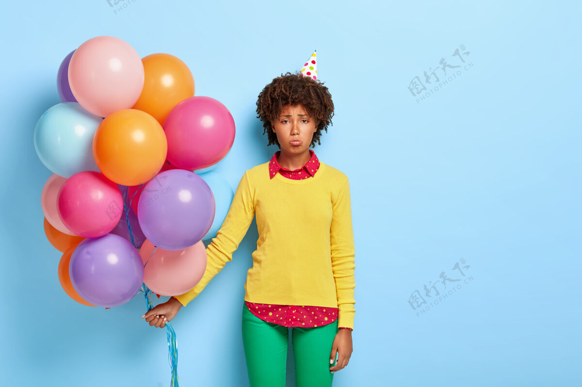 室内失望的女人拿着五颜六色的气球 穿着黄色毛衣摆姿势生日女孩女人