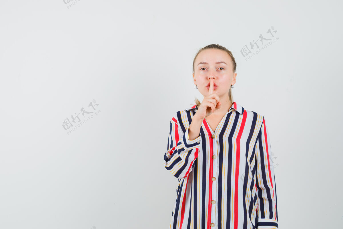 女性穿条纹上衣的年轻女子把手指放在嘴唇上 努力保持沉默 看起来很漂亮年轻衬衫尝试