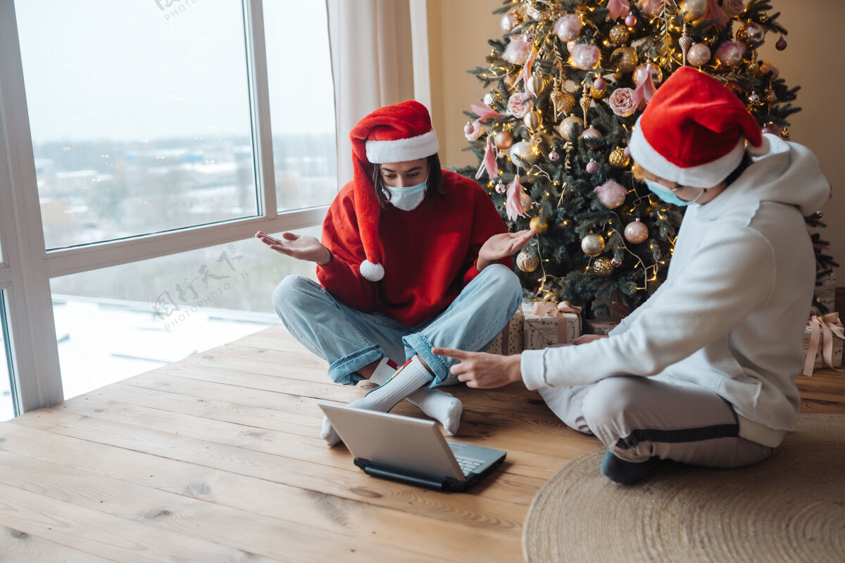 视频两个戴着圣诞帽的朋友在笔记本电脑旁通过视频通话进行互动在家里过圣诞节是一种与世隔绝的生活在假期里是一种社交距离帮助交谈男人