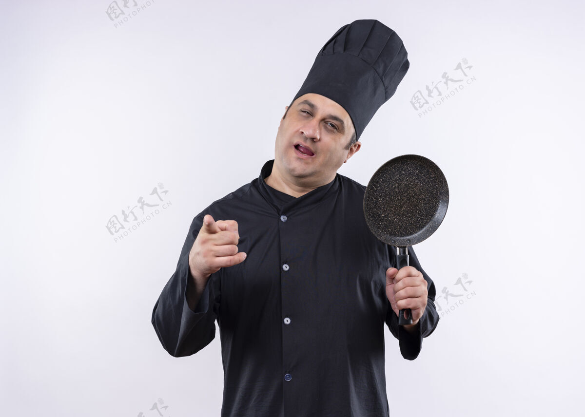 指着男厨师身穿黑色制服 头戴厨师帽 拿着平底锅 手指指着镜头 快乐而积极地站在白色背景上帽子站着烹饪