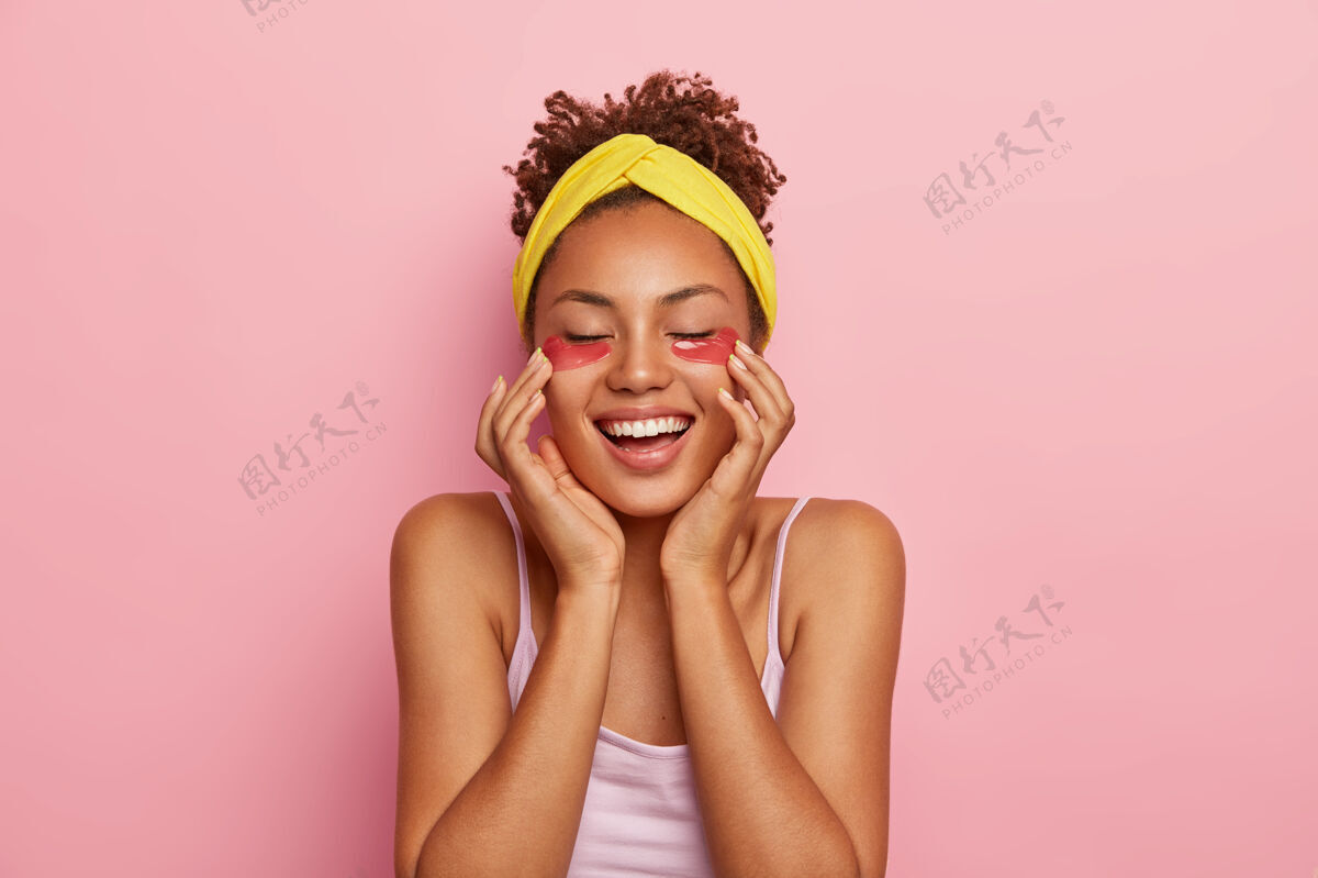 罗西人 种族 快乐 美丽和满足开朗的黑皮肤年轻女子应用水凝胶片 减少皱纹和黑眼圈 头戴黄色头带 有新鲜的皮肤牙齿粉色高兴
