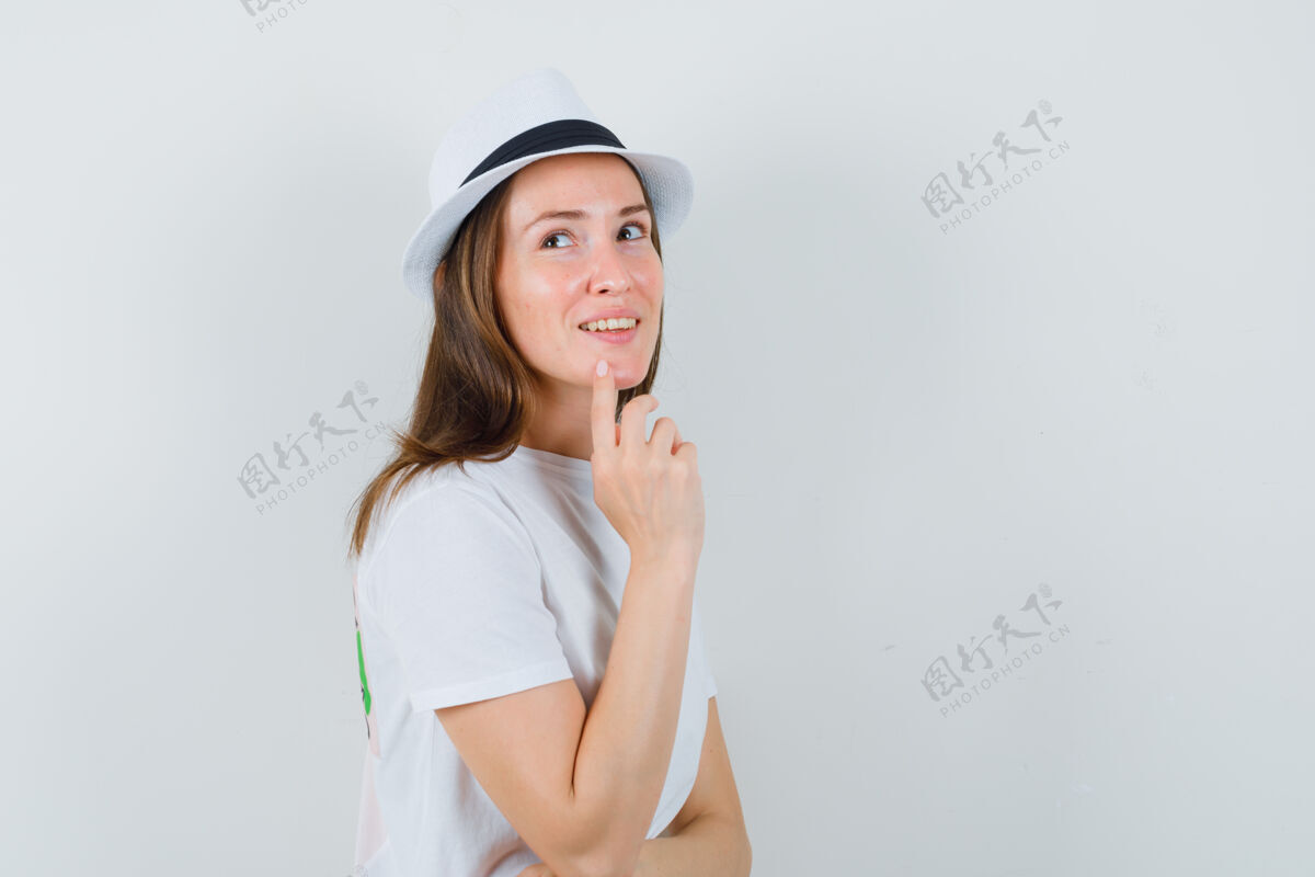 成人穿着白色t恤 戴着帽子 手指放在下巴上的年轻女子 看起来很梦幻肖像可爱休闲