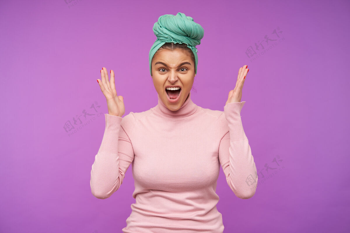 女性压力重重的棕色头发的年轻女子穿着粉色的卷领毛衣 情绪激动地抬起手掌 愤怒地尖叫着 站在紫色的墙上恼怒室内配饰