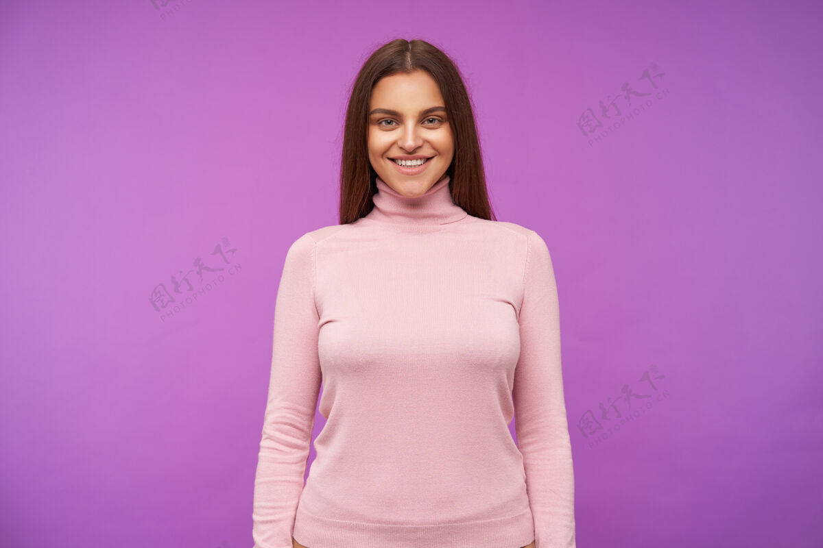 室内室内镜头：年轻的长发黑发女士带着迷人的微笑积极地注视着前方 站在紫色的墙上 双手放低发型爱化妆