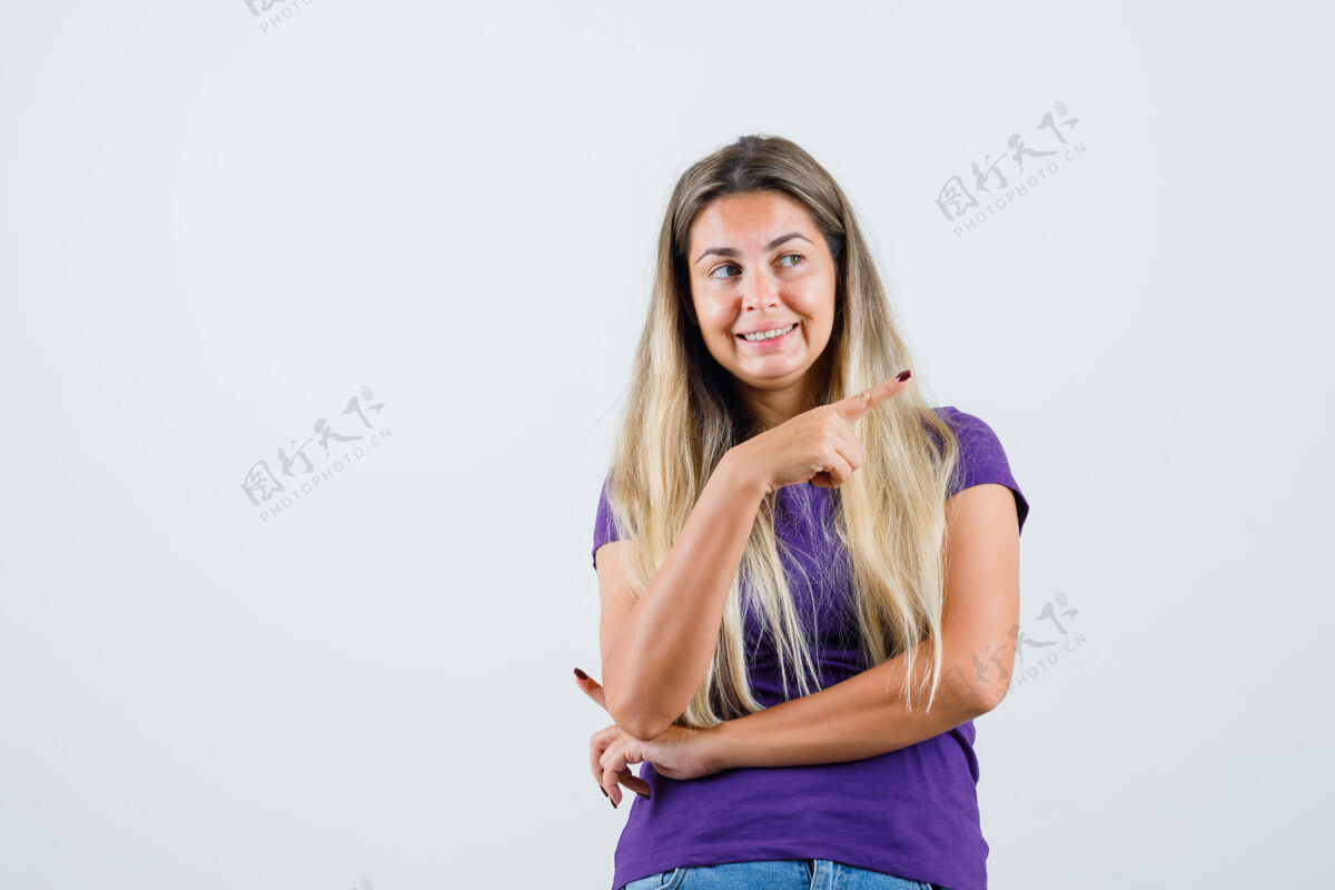 女人金发女郎指着远处 穿着紫色t恤 牛仔裤 看上去很快乐正视图时尚爱看
