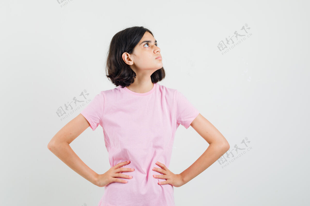 漂亮小女孩抬起头 手放在腰上 穿着粉色t恤 看起来很专注 正面视图向上青年未成年