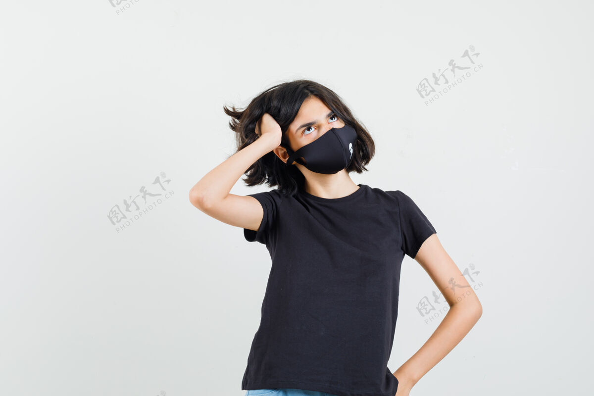 时尚小女孩站在黑色t恤里 戴着面具 面带沉思 摆出一副正面的样子年轻沉思站