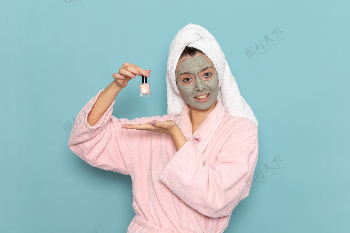 人正面图穿着粉色浴袍的年轻女性拿着指甲油在蓝色的墙上清洗美丽干净的水自我护理霜淋浴奶油成人举行