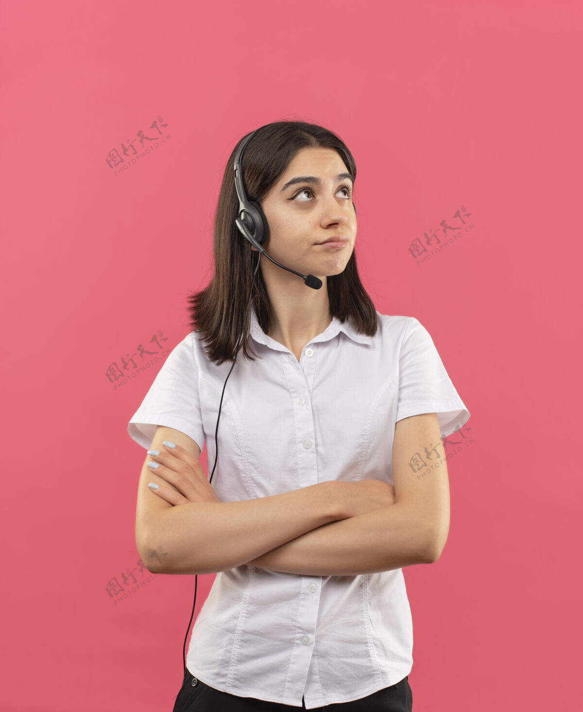 表情一个穿着白衬衫戴着耳机的年轻女孩站在粉红色的墙上 神情沉思地看着一边沉思女孩站着