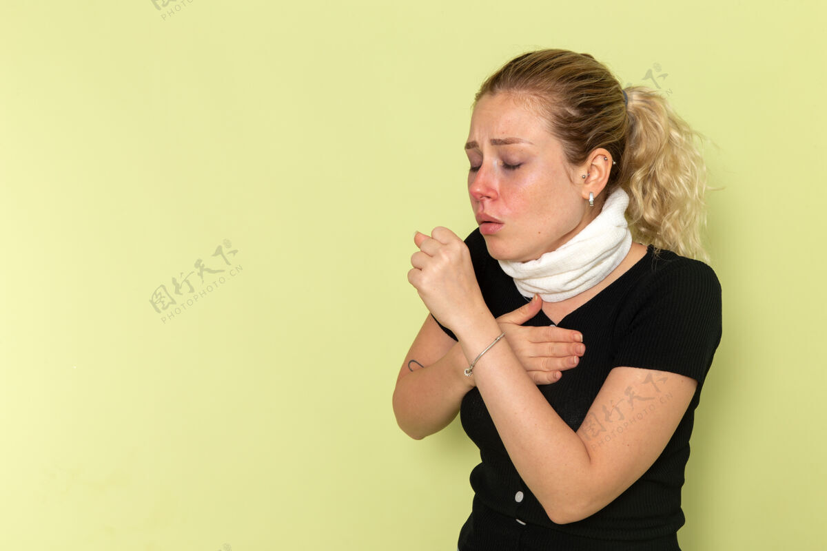 加强正面图年轻女子用白毛巾捂住喉咙 感觉很不舒服 咳嗽在绿墙上生病生病 女性颜色健康毛巾生病女性