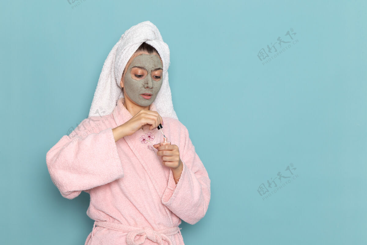 淋浴正面图年轻女性穿着粉色浴袍淋浴后拿着指甲油在蓝色墙壁上美容水霜自理淋浴年轻人浴袍尺子