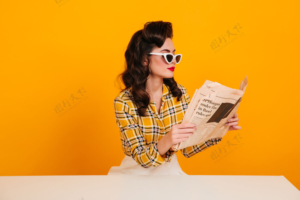 肖像优雅的年轻女子在看报纸摄影棚拍摄的黄色背景下 一个小女孩摆姿势明亮专注格子衬衫