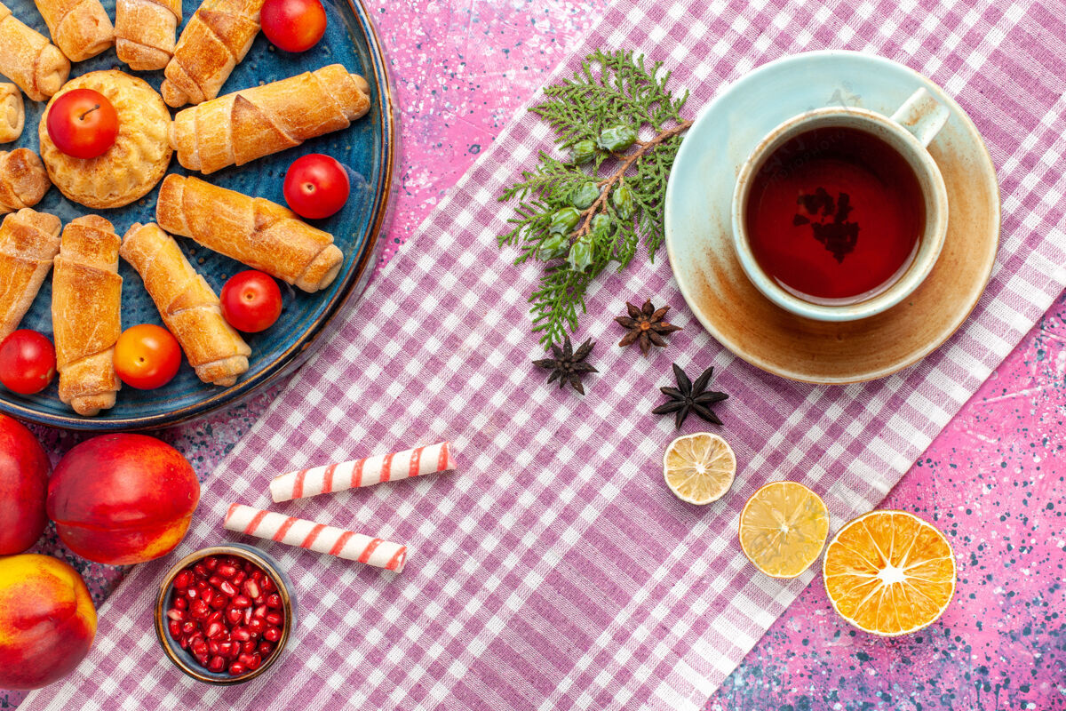 餐厅顶视图甜美美味的百吉饼在托盘内与李子新鲜桃子和一杯茶在淡粉色的桌子上托盘里面饼干