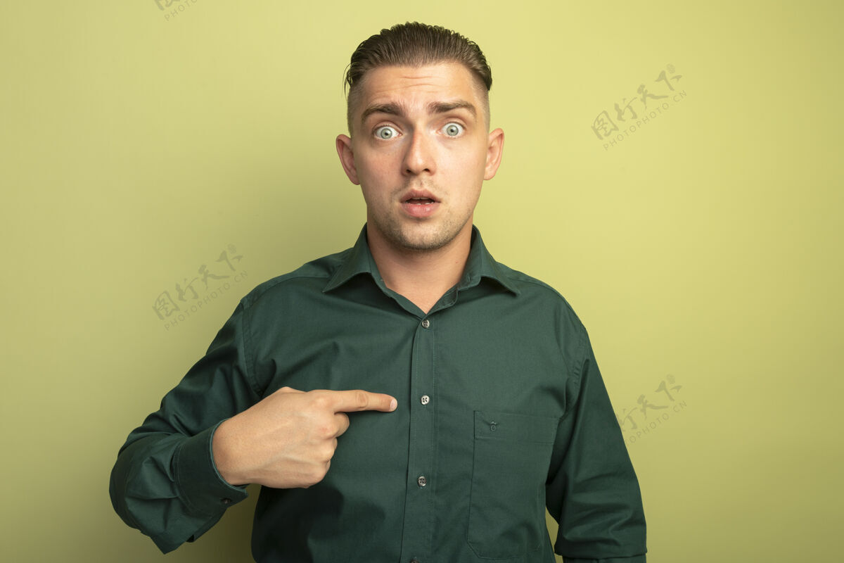 帅哥一个穿着绿衬衫的年轻帅哥站在光墙上指着自己困惑的样子绿困惑他自己