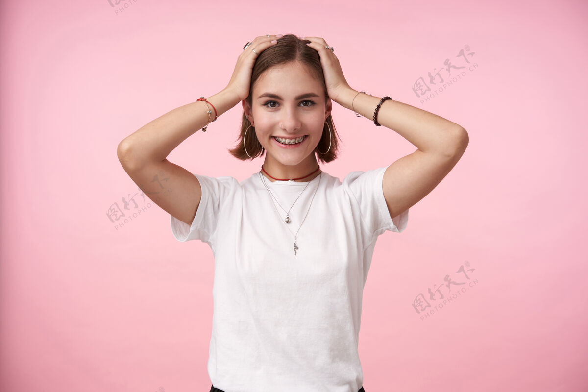 宽松一个年轻迷人的黑发女子站在粉红色的墙上 双手放在头上 面带微笑 正面看着前方手快乐情绪