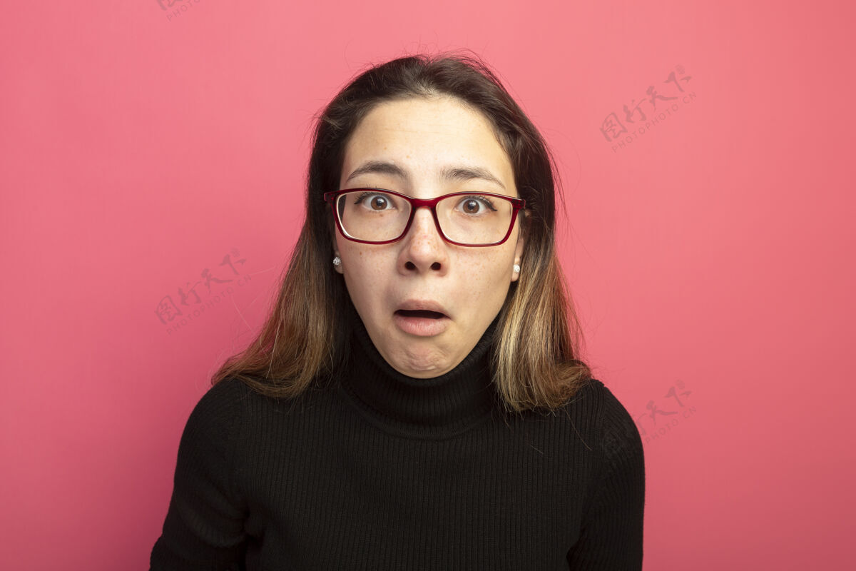 人年轻漂亮的女人穿着黑色高领毛衣 戴着眼镜 站在粉红色的墙上 正困惑地看着前面高领毛衣漂亮黑色