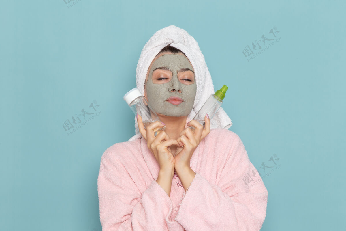 浴室正面图年轻女性穿着粉色浴袍淋浴后手持喷雾在浅蓝色墙壁上美容水霜自助淋浴浴室女自我照顾前
