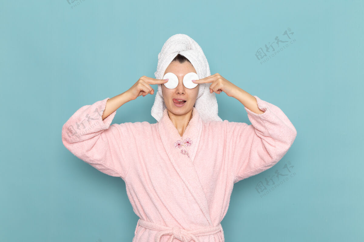 前正面图：年轻女性 穿着粉色浴袍 淋浴后用浅蓝色墙壁上的棉花遮住眼睛 美丽的水 自我护理 淋浴干净男自理盖
