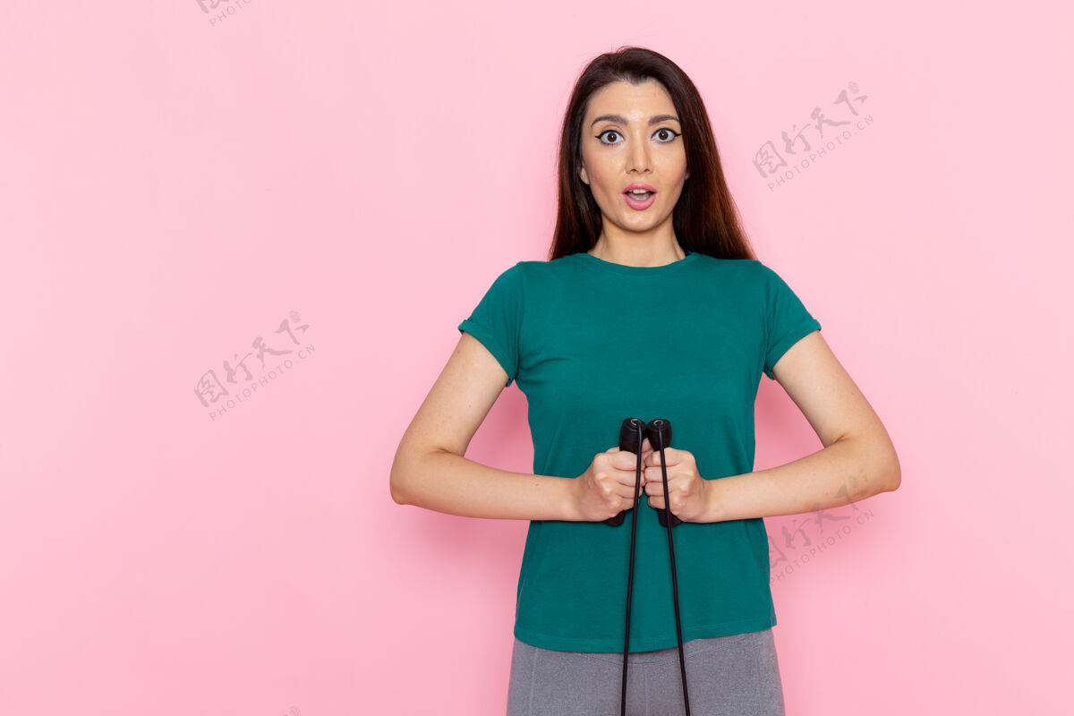 跳过正面图身着绿色t恤的年轻女性手持浅粉色桌上的跳绳腰部运动锻炼美丽苗条女性运动前面运动肖像
