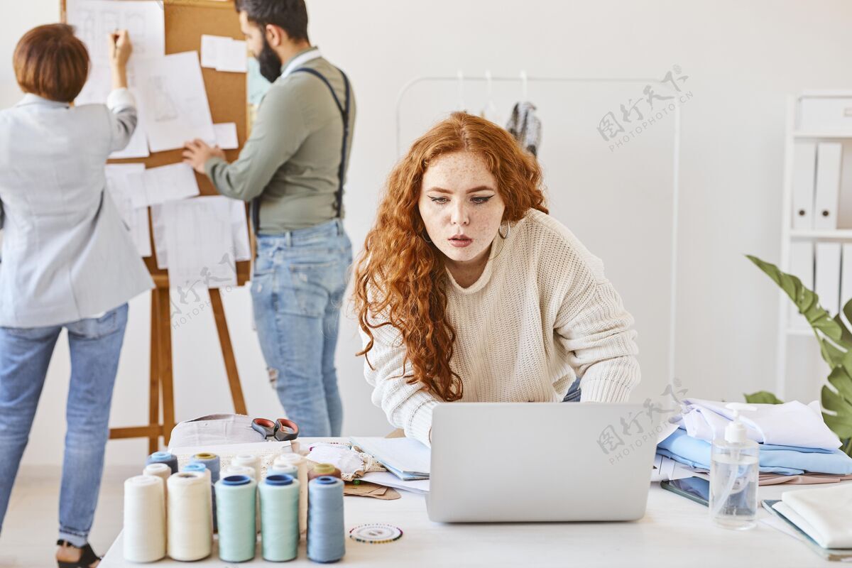 设备女时装设计师与笔记本电脑和同事在工作室工作的正面图Outfitter男性笔记本电脑