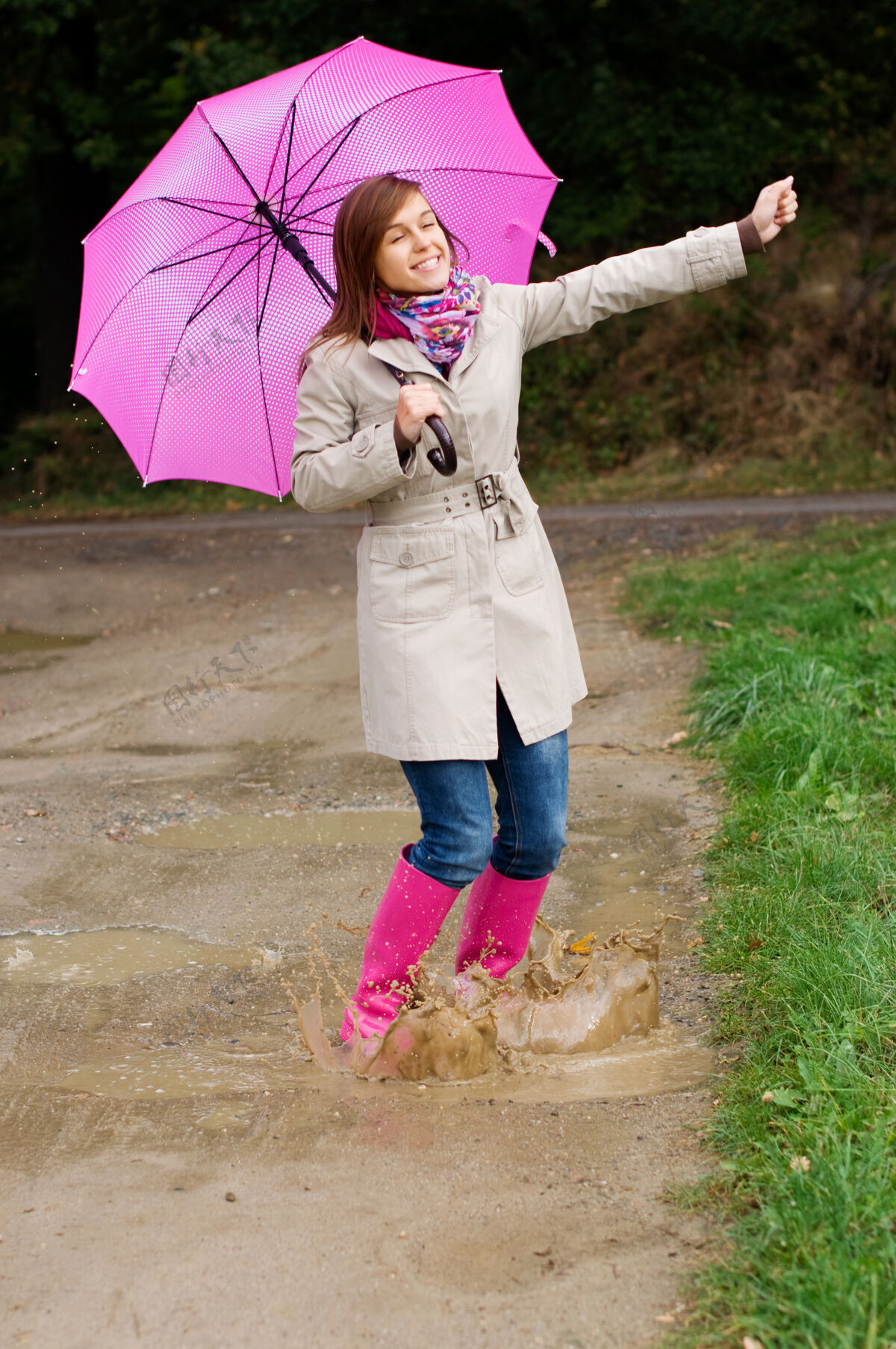 喷雾穿胶靴的年轻女子在雨天玩得开心风衣湿活力