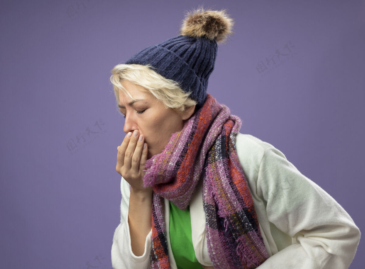 痛苦生病的不健康的女人 短发 戴着暖和的围巾和帽子 站在紫色的墙上 感觉不舒服 咳嗽 流感咳嗽女人感觉