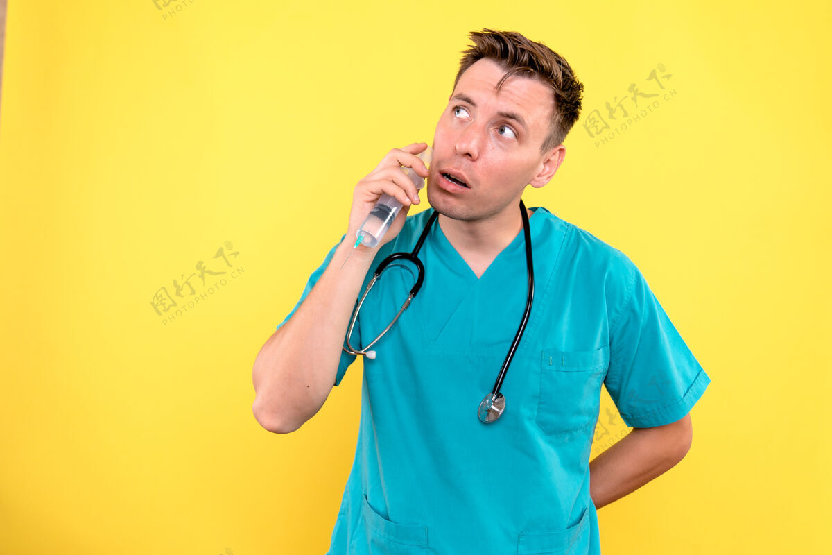 器械黄色墙上拿着针剂的男医生的正视图人医学医院