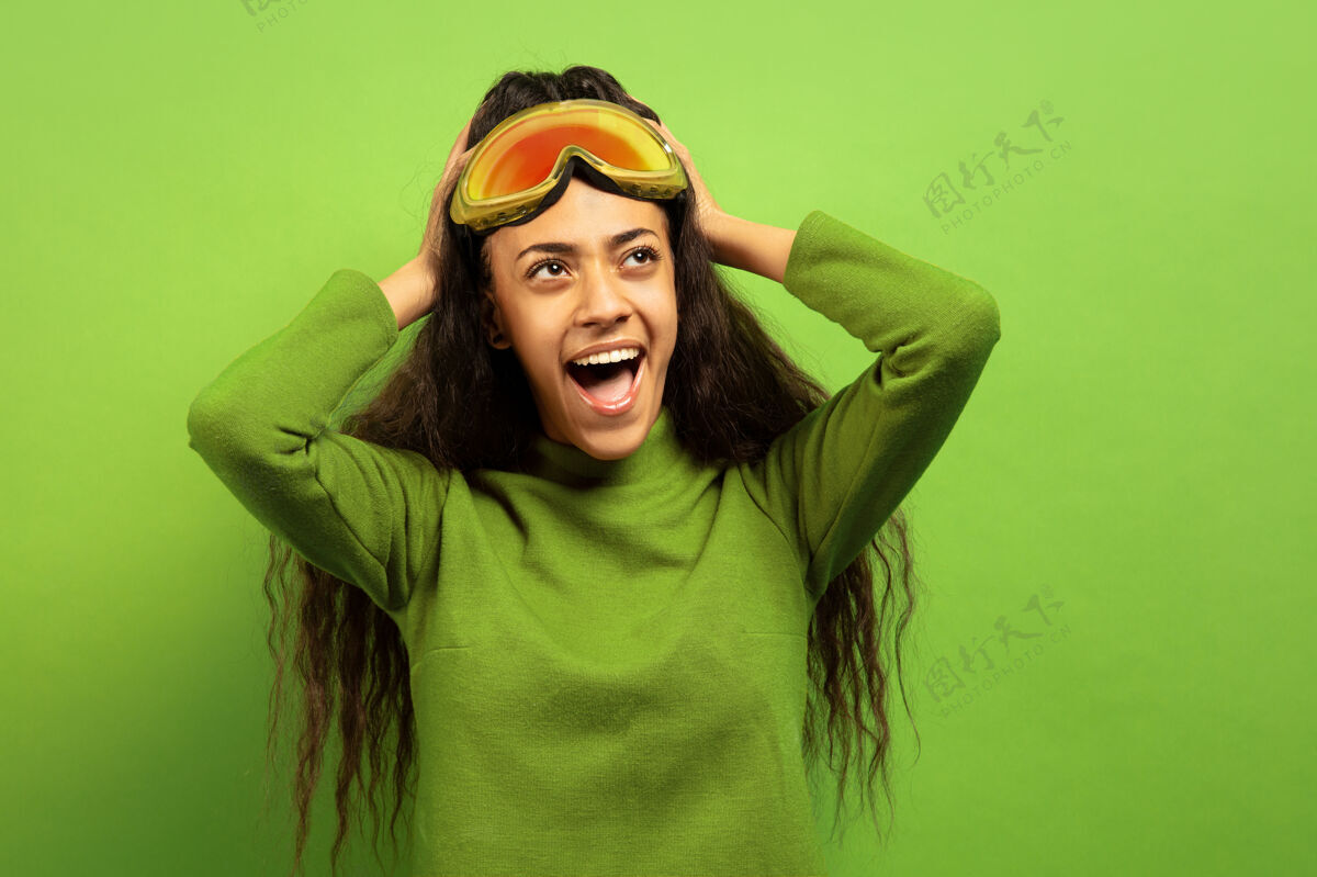 情感以绿色工作室为背景 黑色皮肤的非洲裔年轻女子的滑雪面具肖像人类情感的概念 面部表情 销售 广告 冬季运动和假日惊异的尖叫眼镜肖像黑发