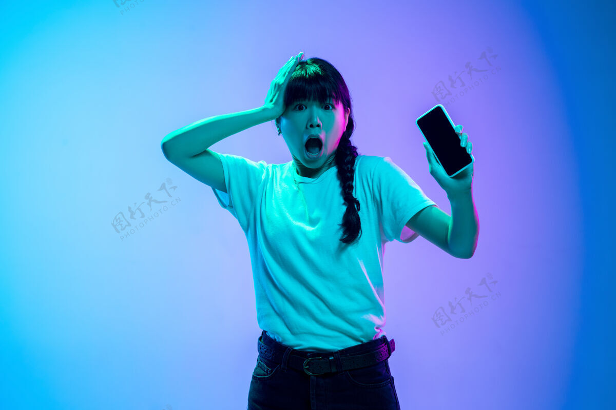 霓虹灯在霓虹灯下的渐变蓝紫色工作室背景上的年轻亚洲女性肖像青春概念 人类情感 面部表情 销售 广告美丽的深褐色模特设备人类人