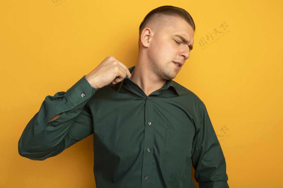 领穿着绿衬衫的年轻帅哥站在橘色的墙上 看着困惑和不高兴地整理衣领站面部表情困惑