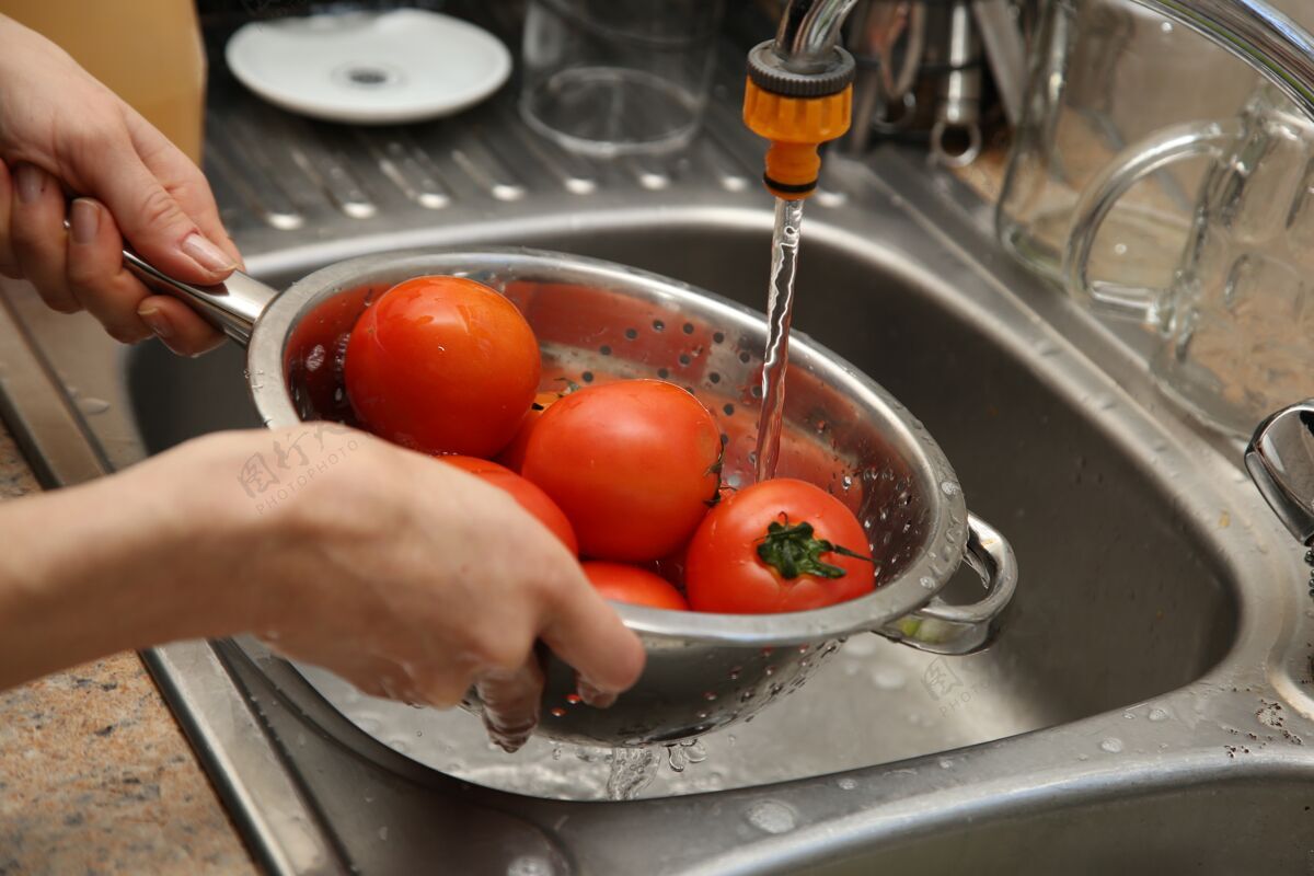 西红柿一个女人用滤水管和厨房水槽洗西红柿蔬菜准备预防